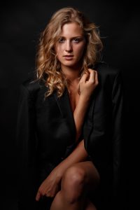 In this captivating photograph, a stunning blonde model exudes confidence and power as she crosses her legs while wearing nothing but a sleek blazer. The subtle lighting highlights her curves and draws attention to the intricate details of the blazer, which lends an air of sophistication to the overall image. Despite the lack of revealing clothing, the model's natural beauty and poise shine through, making this an unforgettable portrait.