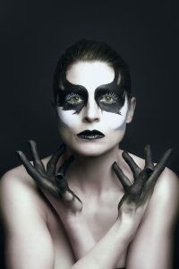 In this striking image, a model with black and white makeup is captured in a dramatic pose, showcasing the contrast between her pale skin and dark hands. The monochromatic makeup creates a bold and powerful effect, emphasizing the model's features and adding depth to the composition. With the photographer's expert use of lighting and posing, this image exudes confidence and sophistication, while showcasing the model's unique beauty and individuality. It's an exceptional example of contemporary fashion photography and portraiture, sure to captivate and inspire.